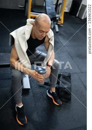Man resting after workout with protein shake in modern gym Man resting after workout with protein shake in modern gym 136961022