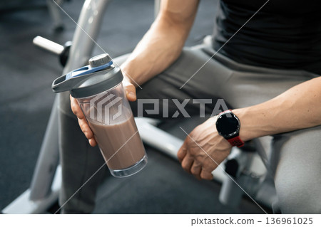 Man holding chocolate protein drink in gym Man holding chocolate protein drink in gym 136961025