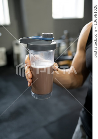 Man holding protein shaker bottle close up in gym interior Man holding protein shaker bottle close up in gym interior 136961026