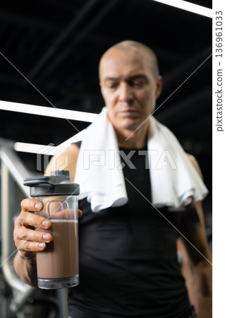 Man holding protein shaker bottle close up in gym Man holding protein shaker bottle close up in gym 136961033