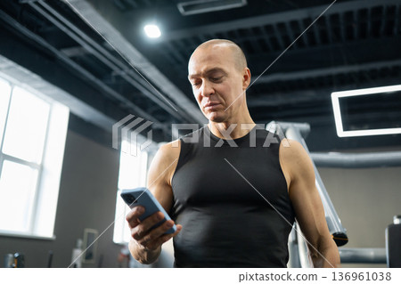 Man using smartphone during workout break in gym Man using smartphone during workout break in gym 136961038
