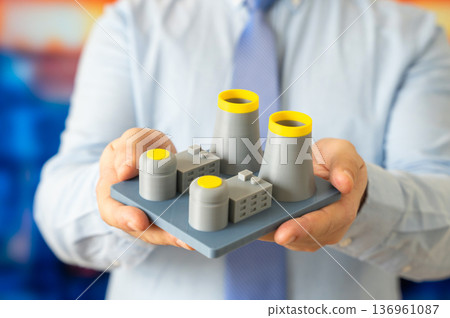A man holds a model of a nuclear power plant. Nuclear energy and electricity generation. Atomic power development and sustainable energy strategy 136961087