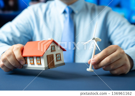 House and windmill in the hands of a man. Autonomous housing powered by renewable energy. Sustainable living and home independence. Green technology for households and energy efficiency House and windmill in the hands of a man. Autonomous housing powered by renewable energy. Sustainable living and home independence. Green technology for households and energy efficiency 136961162