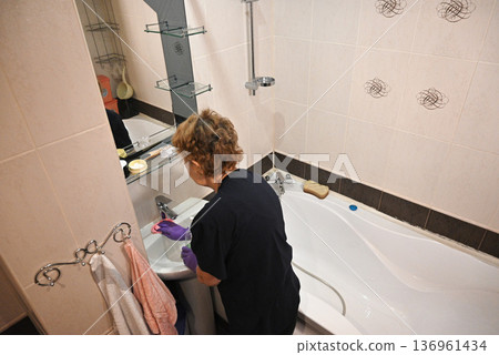 Woman cleaning bathtub in bathroom during afternoon Woman cleaning bathtub in bathroom during afternoon 136961434
