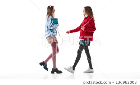 Two teenage girls in preppy outfits walking toward each other isolated on white. 136962008