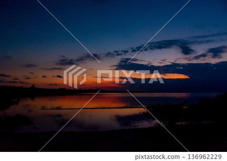 Dramatic sunset reflecting on calm lake waters at dusk Dramatic sunset reflecting on calm lake waters at dusk 136962229