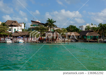 Tropical waterfront with thatched roof huts and docked boats Tropical waterfront with thatched roof huts and docked boats 136962292