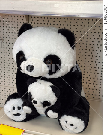 Plush panda toy holding smaller panda on shelf. Childhood comfort, gift idea, innocence concept, retail display, softness and tenderness 136962394