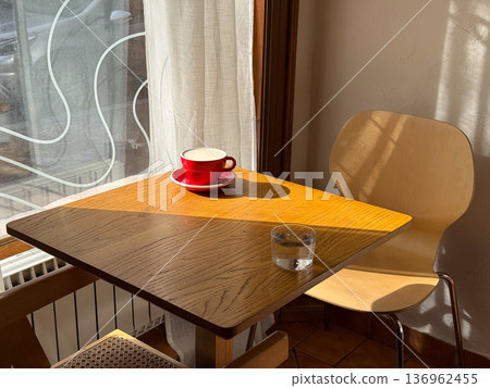 Red coffee cup on wooden table in sunlight. Caffeine break, cafe interior, breakfast, warmth, relaxation moment Red coffee cup on wooden table in sunlight. Caffeine break, cafe interior, breakfast, warmth, relaxation moment 136962455