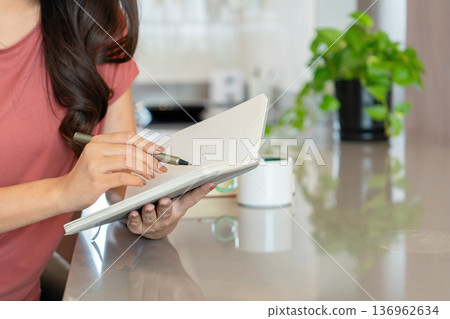 Smiling Asian Woman Writing in Notebook with Coffee 136962634