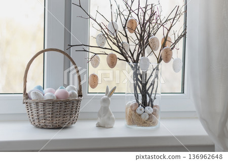 Easter basket and branches with decorative eggs on windowsill 136962648