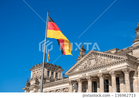 Berlin, germany, august 15, 2023. The german national flag waving in front of the historic reichstag building under a clear blue sky, symbolizing government and democracy 136962713