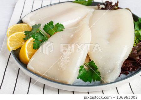 Fresh squid on a black plate with greens and lemon slices prepared for cooking in a kitchen setting Fresh squid on a black plate with greens and lemon slices prepared for cooking in a kitchen setting 136963002