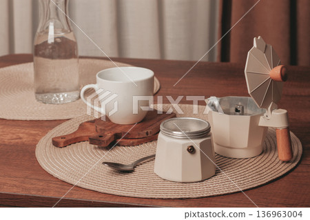 Coffee brewing setup on a rustic wooden table with a cup and water bottle in the morning light 136963004