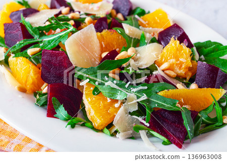 Fresh salad with beets, oranges, and arugula topped with cheese and nuts served on a white plate Fresh salad with beets, oranges, and arugula topped with cheese and nuts served on a white plate 136963008