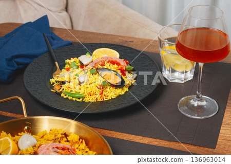 Dinner table with seafood paella and drink in a cozy setting during the evening hours Dinner table with seafood paella and drink in a cozy setting during the evening hours 136963014