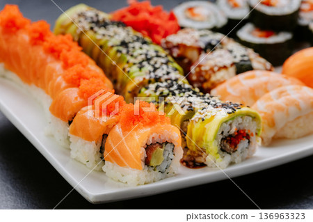 Assorted sushi rolls nigiri and sashimi served on white plate over dark background Assorted sushi rolls nigiri and sashimi served on white plate over dark background 136963323