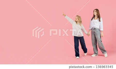 Little girl pointing forward on pink studio background and holding mothers hand 136963345