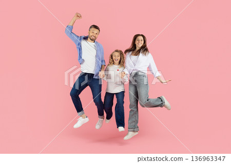 Happy caucasian family jumping together on pink studio background, holding hands 136963347