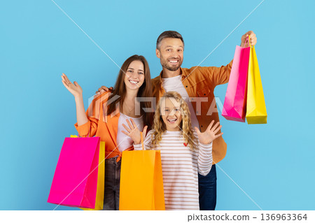 Cheerful family posing with bright shopping bags on blue background 136963364