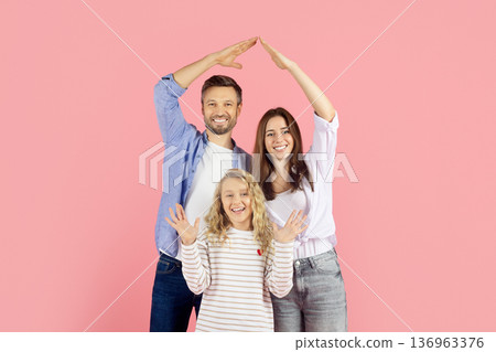 Caucasian parents forming house shape with hands above daughter on pink background Caucasian parents forming house shape with hands above daughter on pink background 136963376