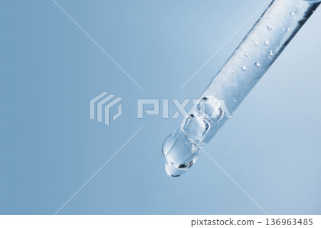 Pipette dropper extracting clear transparent liquid with bubbles against blue background Pipette dropper extracting clear transparent liquid with bubbles against blue background 136963485