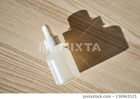Dropper bottle with serum casting shadow on wood 136963525