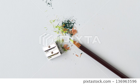Colored pencil and metal sharpener on a white background. Wood shavings and colored pigment on a white table. Colored pencil and metal sharpener on a white background. Wood shavings and colored pigment on a white table. 136963596