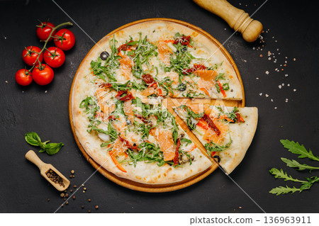 Gourmet pizza with salmon arugula cheese and sun dried tomatoes on wooden board Gourmet pizza with salmon arugula cheese and sun dried tomatoes on wooden board 136963911