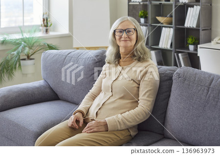 Happy confident senior woman sitting on home sofa in relaxing pose to enjoy carefree day with smile 136963973