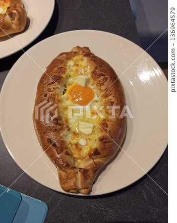 Georgian khachapuri with egg cheese and butter served on white plate. Traditional bakery concept of homemade cuisine comfort food and national dish Georgian khachapuri with egg cheese and butter served on white plate. Traditional bakery concept of homemade cuisine comfort food and national dish 136964579