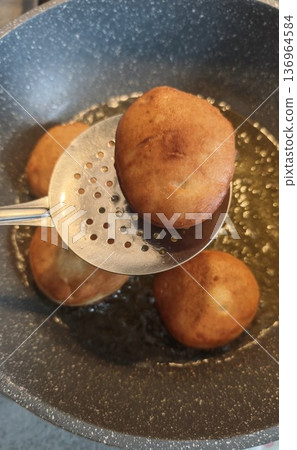 Fried donut cooking in hot oil with skimmer in pan. Close up bakery concept of homemade dessert street food and deep frying process Fried donut cooking in hot oil with skimmer in pan. Close up bakery concept of homemade dessert street food and deep frying process 136964584