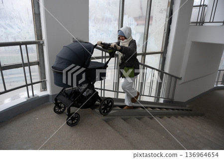 Young mother pushing stroller up residential building stairs Young mother pushing stroller up residential building stairs 136964654