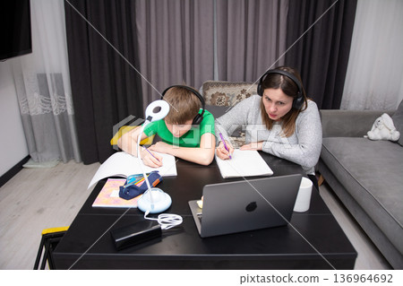 Learning together during online classes at home in a cozy living room setting with a child and parent engaged in schoolwork, showcasing dedication and focus in education Learning together during online classes at home in a cozy living room setting with a child and parent engaged in schoolwork, showcasing dedication and focus in education 136964692
