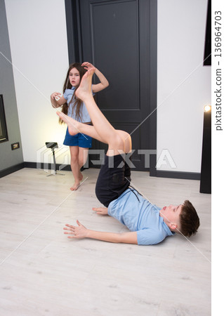 Children playing together in a cozy indoor space while practicing funny gymnastics moves on smooth wooden flooring during a playful afternoon activity Children playing together in a cozy indoor space while practicing funny gymnastics moves on smooth wooden flooring during a playful afternoon activity 136964703