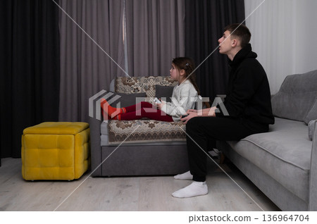 Siblings enjoying a cozy gaming night together in their living room while immersed in an exciting virtual adventure during the cool evening hours 136964704
