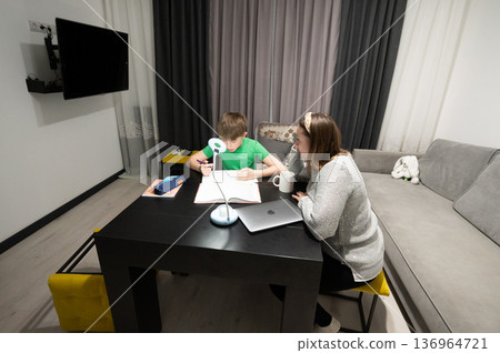 Homework assistance at a cozy living room table in a modern home during evening hours fostering learning and connection between mother and son Homework assistance at a cozy living room table in a modern home during evening hours fostering learning and connection between mother and son 136964721