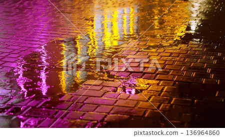 Rain drops in puddle on cobblestone street with pink orange night lights. Moody, futuristic vibes. Rain drops in puddle on cobblestone street with pink orange night lights. Moody, futuristic vibes. 136964860