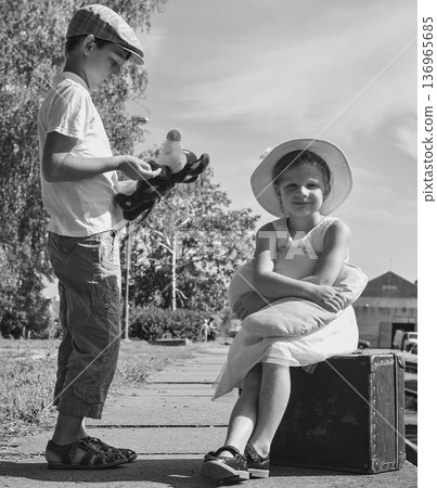 Little children - girl and boy on a railway station, waiting for the train with vintage suitcase. Traveling, holiday and chilhood concept. Travel insurance concept. Travel, tourism, summer vacation 136965685