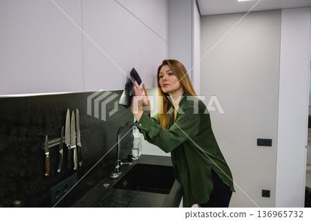 Woman dusting kitchen cabinet with cloth 136965732