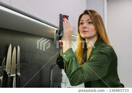 Woman dusting kitchen cabinet with cloth 136965733
