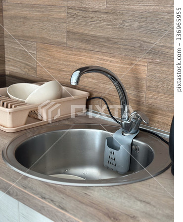 Kitchen sink with faucet and dish rack in modern interior. Household routine, cleanliness and domestic functionality concept. Kitchen sink with faucet and dish rack in modern interior. Household routine, cleanliness and domestic functionality concept. 136965955