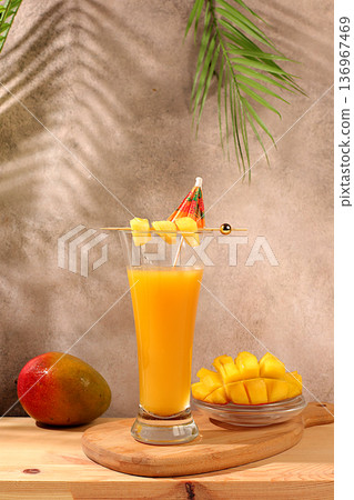 Homemade cocktail, juice, or lemonade with mango slices and ice on a sun-drenched kitchen table. Summer party concept. Refreshing summer diet drink recipe, detox diet and healthy lifestyle, 136967469