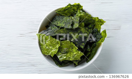 Top view of crispy seaweed chips in white bowl, minimalist food photography on light wooden background 136967626