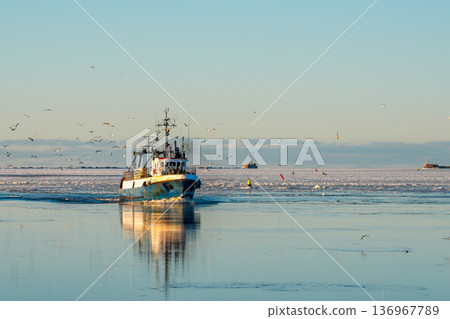 Fishing Vessel Returning to Liepaja Port Across Icy Baltic Sea at Golden Winter Sunset Fishing Vessel Returning to Liepaja Port Across Icy Baltic Sea at Golden Winter Sunset 136967789