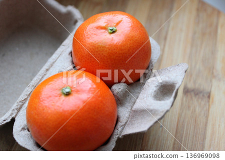 Breakfast For Two Concept Stock Photo. Two fresh mandarins in paper container on wooden planks surface Breakfast For Two Concept Stock Photo. Two fresh mandarins in paper container on wooden planks surface 136969098