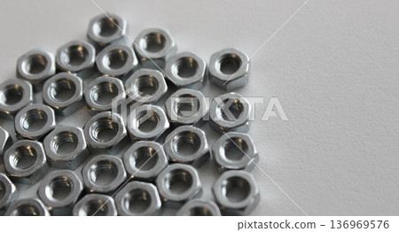 Hex nuts on a flat surface are huddled together on the left side of the image Hex nuts on a flat surface are huddled together on the left side of the image 136969576