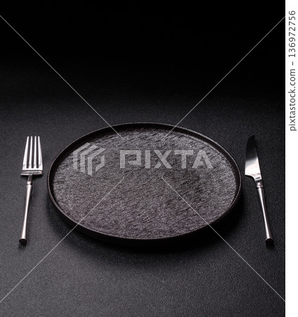 An empty round ceramic plate, knife, and fork as a dining table setting. An empty plate 136972756