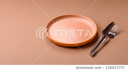 An empty round ceramic plate, knife, and fork as a dining table setting. An empty plate 136972757