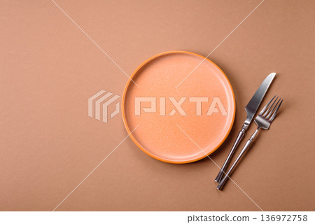 An empty round ceramic plate, knife, and fork as a dining table setting. An empty plate 136972758